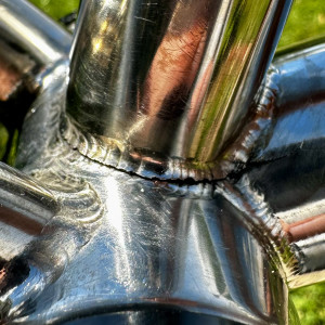 A silver bike frame cropped to show the bottom bracket area with a crack in the weld and downtube