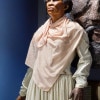 A wax statue of an older black woman with short graying hair in a simple cream shirt and skirt with a pink shawl stands looking up to the sky.