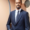 A wax statue of a tall, thin, good-looking black man with a mustache and goatee wearing a navy blue suit.