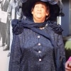 A wax statue of a black woman in a beautiful dark blue hat and matching dress looks up and to her right with a calm and hopeful expression.