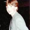 A red-haired 17-year-old boy with very feathered red hair is pictured from his left as he turns to face the camera smiling while wearing a tweed sport coat with several pins on the lapel.