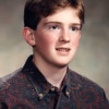 A 17-year-old boy with freckled pink chubby cheeks and red hair looks off to the right while wearing a paisley shirt.